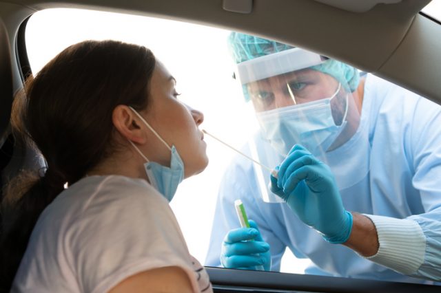 Woman getting tested at a coronavirus drive thru station by medical staff with PPE suit by throat swab. Health care drive thru service and medical concept